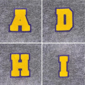 May include: Four individual patches displaying the letters A, D, H, and I. Each letter is yellow with a purple border, set against a grey background. The letters are in a classic varsity style.