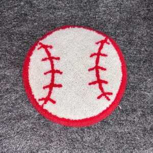 May include: A circular baseball-themed item with a white central area and a red border. Red stitching details are visible, replicating a baseball's design. This item is likely a coaster or patch, suitable for sports fans.