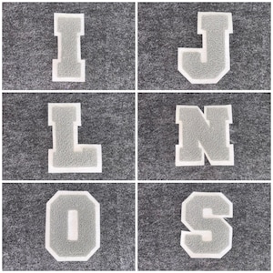May include: Six gray and white varsity letter patches: I, J, L, N, O, and S. Each letter has a textured grey centre with a white border. The letters are displayed on a grey felt background.
