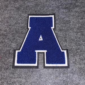May include: A large, blue letter "A" patch with a white border and a small white triangle in the centre. The patch is on a grey background.