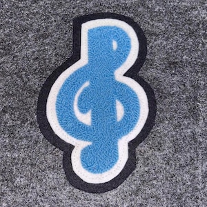 May include: A blue treble clef patch with a white border and a black outline. The musical symbol is embroidered on a grey background. The patch is a musical accessory.