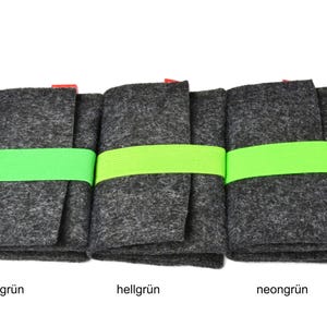 May include: Three rectangular dark gray felt cases, each secured with a bright neon green elastic band. The cases are arranged side-by-side, and each features a small red tag at the top edge. Below each case, the text reads gr&uuml;n, hellgr&uuml;n, and neongr&uuml;n.