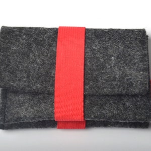 以下が含まれることがあります： 赤いストラップと「HAND MADE」と書かれた赤いラベルが付いた灰色のフェルトポーチです。