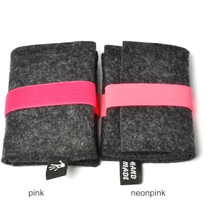 May include: Two rectangular dark gray felt cases secured with bright pink elastic bands. Each case features a small black fabric tag at the bottom edge. The left tag displays a white hand icon, while the right tag features the text HAND MADE in white.