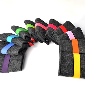 May include: A collection of ten rectangular dark gray felt sleeves arranged in a fan shape. Each sleeve is secured with a vibrant elastic band in colors including purple, blue, light blue, green, lime, pink, red, orange, and yellow.