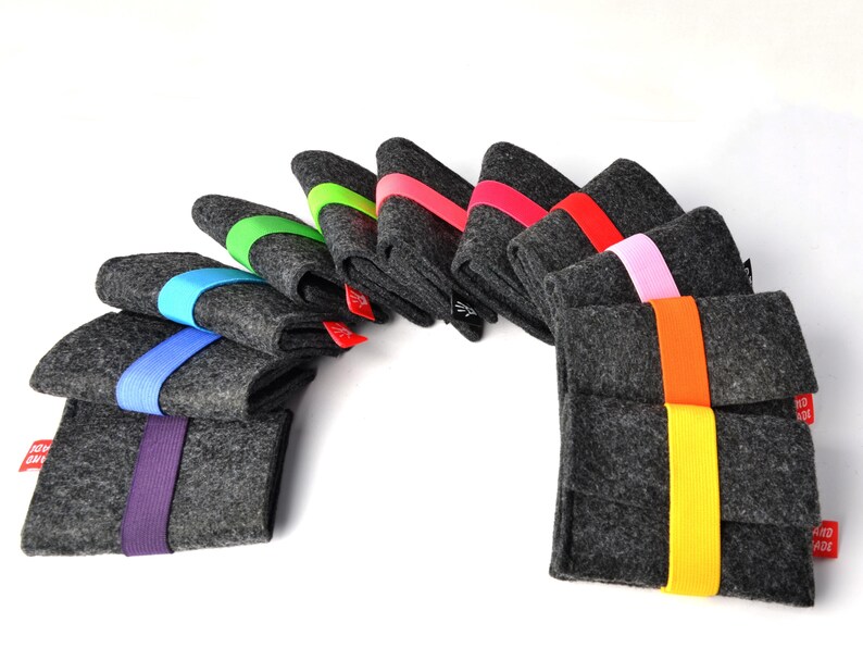 May include: A collection of ten rectangular dark gray felt sleeves arranged in a fan shape. Each sleeve is secured with a vibrant elastic band in colors including purple, blue, light blue, green, lime, pink, red, orange, and yellow.