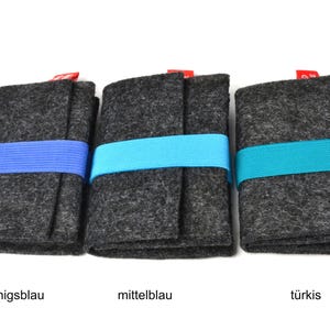May include: Three rectangular dark gray felt cases, each secured with a horizontal elastic band. The bands are colored royal blue, medium blue, and turquoise from left to right. Each case features a small red fabric tag at the top edge.