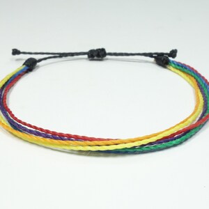 May include: A rainbow colored friendship bracelet made of woven string with a black adjustable closure.