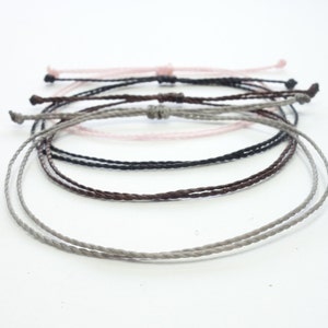 May include: A set of four braided cord bracelets in gray, brown, black, and pink.