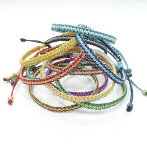 K&ouml;nnte beinhalten: Ein Stapel bunter geflochtener Armb&auml;nder mit verschiedenen farbigen Streifen. Die Armb&auml;nder sind aus d&uuml;nnem Kordel gefertigt und haben ein einfaches Knotendesign.
