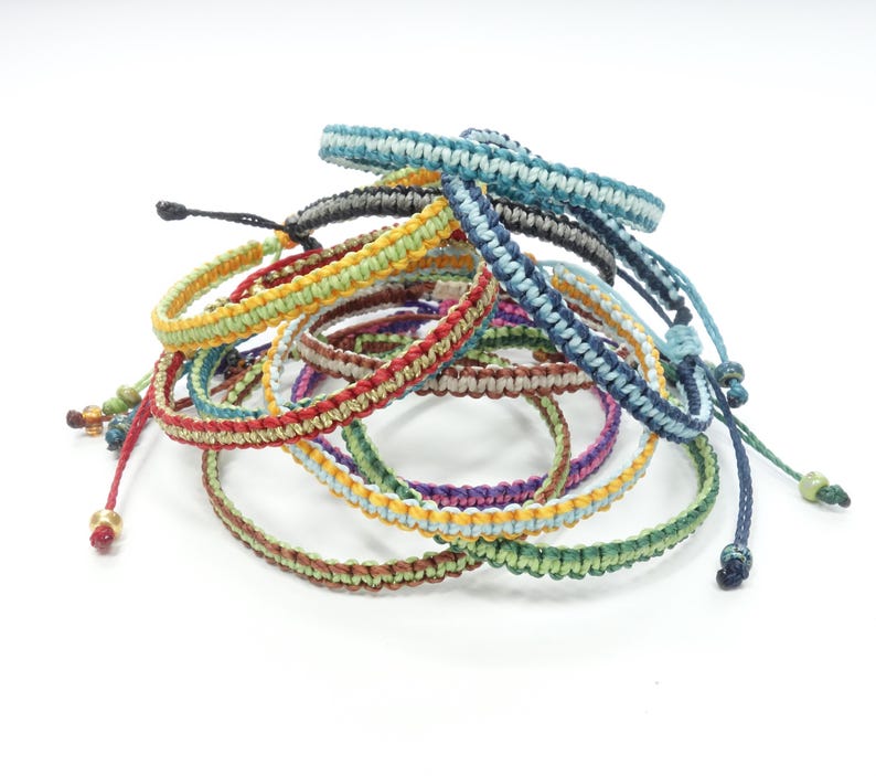 K&ouml;nnte beinhalten: Ein Stapel bunter geflochtener Armb&auml;nder mit verschiedenen farbigen Streifen. Die Armb&auml;nder sind aus d&uuml;nnem Kordel gefertigt und haben ein einfaches Knotendesign.