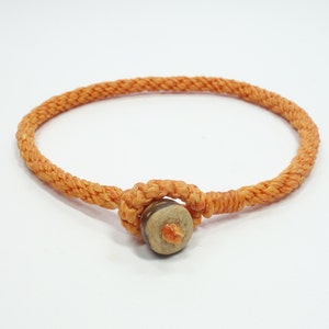 May include: An orange braided bracelet with a wooden bead in the center.