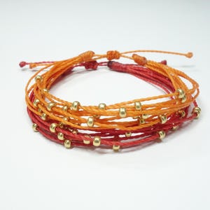 May include: A multi-strand bracelet with red and orange string and gold beads.