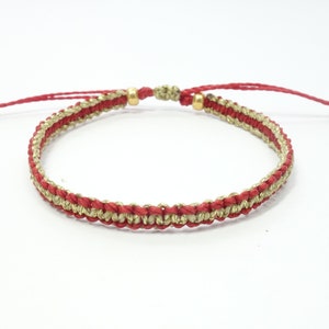 Può includere: Bracciale in macramè rosso e oro con chiusura scorrevole regolabile. Il bracciale presenta un design intrecciato con fili rossi e oro, e perline color oro alle estremità. Un accessorio semplice ed elegante.