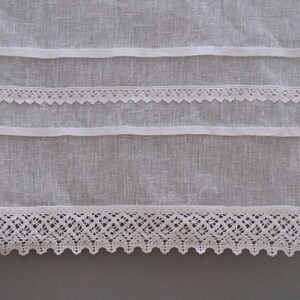 Peut inclure: Gros plan sur un textile en lin blanc avec des rang&eacute;es horizontales d'&eacute;l&eacute;ments d&eacute;coratifs. Le motif pr&eacute;sente des bandes de tissu et une d&eacute;licate garniture en dentelle. La dentelle a un bord festonn&eacute;, ajoutant une touche d'&eacute;l&eacute;gance.