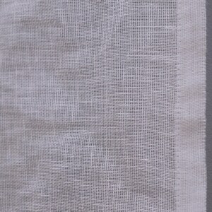 Peut inclure: Gros plan sur un tissu blanc, tiss&eacute; l&acirc;chement. Le tissu pr&eacute;sente un motif quadrill&eacute; et un aspect l&eacute;g&egrave;rement textur&eacute;. Une bordure blanche et propre longe le bord droit du tissu.
