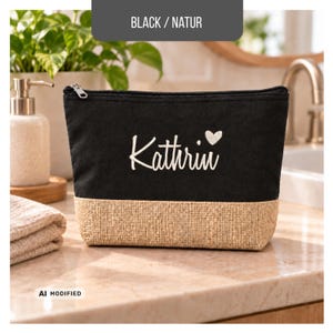 May include: A black zipped pouch with a natural-coloured burlap base. The front features the white embroidered name Kathrin followed by a small white heart. The pouch has a silver-toned metal zip pull and a rectangular shape.