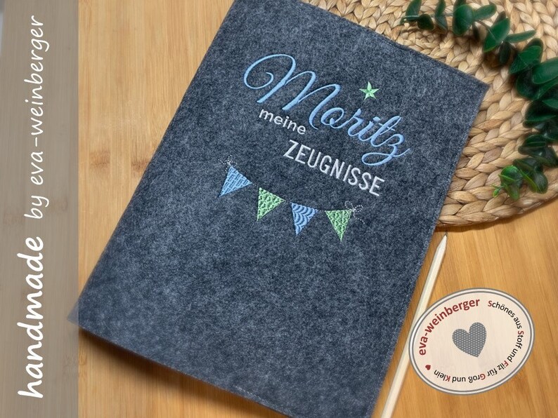 K&ouml;nnte beinhalten: Ein grauer Filzordner mit dem Namen "Moritz" in blauer und wei&szlig;er Schrift bestickt. Der Ordner hat ein blaues und gr&uuml;nes Wimpeldesign und der Text "meine Zeugnisse" ist ebenfalls auf dem Ordner gestickt.