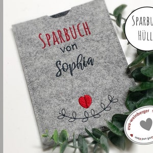 Puede incluir: Cubierta de Sparbuch (libro de ahorros) de fieltro gris con texto bordado en rojo "Sparbuch von Sophia" y un corazón rojo con hojas verdes.