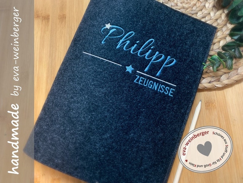 May include: A dark grey felt folder with the name "Philipp" embroidered in blue with two stars and the word "Zeugnisse" below. The folder is handmade by eva-weinberger.
