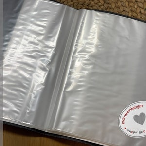 K&ouml;nnte beinhalten: Ein grauer Stoffordner mit durchsichtigen Plastikh&uuml;llen zum Aufbewahren von Papieren. Der Ordner hat ein wei&szlig;es Etikett mit dem Text "handmade by eva-weinberger" und einen kleinen wei&szlig;en Kreis mit dem Text "eva-weinberger" und einem Herz.