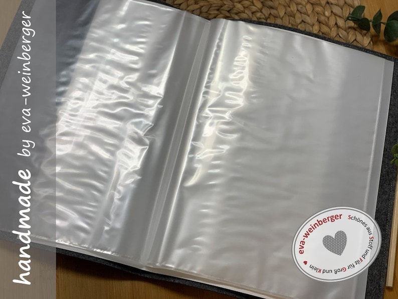 K&ouml;nnte beinhalten: Ein grauer Stoffordner mit durchsichtigen Plastikh&uuml;llen zum Aufbewahren von Papieren. Der Ordner hat ein wei&szlig;es Etikett mit dem Text "handmade by eva-weinberger" und einen kleinen wei&szlig;en Kreis mit dem Text "eva-weinberger" und einem Herz.