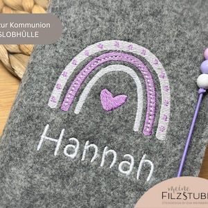 May include: Grey felt case embroidered with a rainbow and a heart, with the name "Hannah" in white. The case has a beaded cord and text that reads "Geschenk zur Kommunion GOTTESLOBHÜLLE".