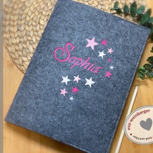 May include: Grey felt folder with pink stars and the name "Sophia" embroidered in pink. The folder has a heart-shaped logo with the text "eva-weinberger" and "Sch&ouml;nes aus Stoff und Filz f&uuml;r Gro&szlig; und Klein".