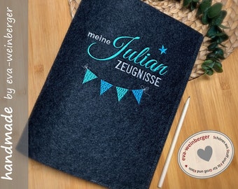 Könnte beinhalten: Ein dunkelgrauer Filzordner mit blauer und türkisfarbener Stickerei. Die Stickerei lautet "meine Julian ZEUGNISSE" mit einem Stern und einer Girlande aus Fahnen.