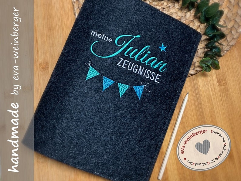 Pu&ograve; includere: Una cartella in feltro grigio scuro con ricami blu e turchese. Il ricamo dice "meine Julian ZEUGNISSE" con una stella e una fila di bandiere.