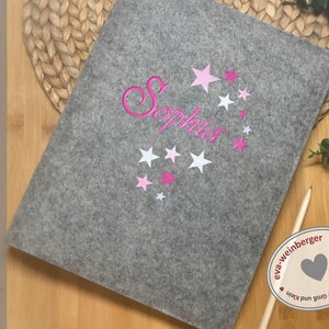 May include: Grey felt laptop sleeve with pink and white stars and the name "Sophia" embroidered on it. The sleeve has a label that says "handmade by eva-weinberger".