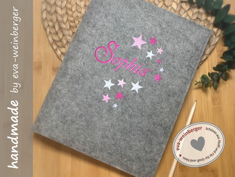 May include: Grey felt laptop sleeve with pink and white stars and the name "Sophia" embroidered on it. The sleeve has a label that says "handmade by eva-weinberger".