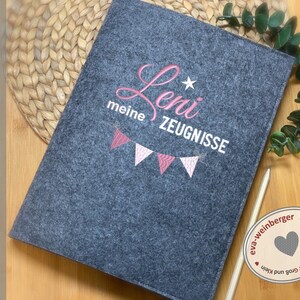May include: Gray felt folder with pink embroidery that says "meine ZEUGNISSE" and "Leni" with a star. The folder is handmade by eva-weinberger.