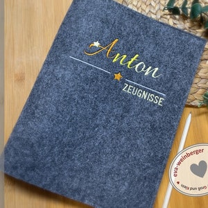 May include: A grey felt folder with the name "Anton" embroidered in yellow thread. The folder also has the word "Zeugnisse" embroidered in yellow thread. The folder is handmade by eva-weinberger.