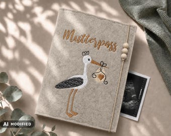 May include: A beige felt cover for a Mutterpass featuring an embroidered stork carrying a bundle with a heart. The cover includes a vertical elastic band with three wooden beads and displays the text Mutterpass in brown cursive embroidery.