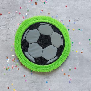 Könnte beinhalten: Ein grüner Filzkreis mit einem schwarzen und grauen Fußball-Design in der Mitte. Der Fußball ist mit weißen Nähten bestickt.
