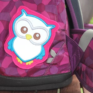 Könnte beinhalten: Ein rosa Rucksack mit einem weißen und blauen Eulen-Patch. Der Rucksack hat ein lila-rosa Blumenmuster.