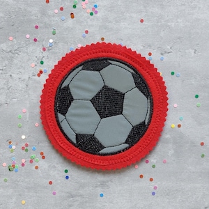 Könnte beinhalten: Roter Filz-Kreis mit einem schwarzen und grauen gestickten Fußball in der Mitte.