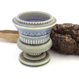 May include: A small, blue and white ceramic planter with a decorative design. The planter is sitting on a piece of bark.