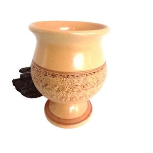 May include: A light brown ceramic cup with a textured design and a wide base. The cup is perfect for serving beverages.