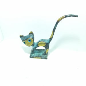 May include: A small, stylized bronze cat figurine with a long, curved tail. The cat is painted in shades of blue and gold, with blue eyes.