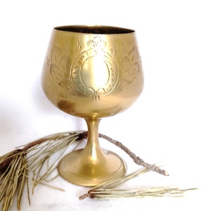 Peut inclure: Un gobelet en laiton doré avec un motif floral gravé. Le gobelet a une large coupe et une tige haute et fine.