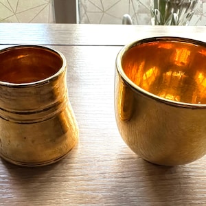 Peut inclure: Deux récipients en céramique dorés. L'un est une tasse avec une anse, l'autre est un bol. Les deux ont une surface texturée et un éclat métallique. La tasse mesure environ 10 cm de haut, et le bol mesure environ 8 cm de haut.