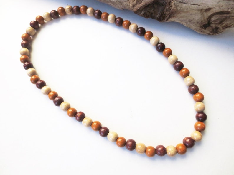 May include: A brown, beige, and cream colored wooden bead necklace. The beads are round and strung together on a cord.