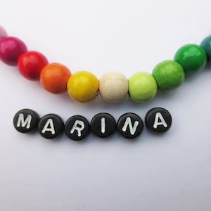 May include: A rainbow colored wooden bead necklace with the name "MARINA" spelled out in black letter beads.