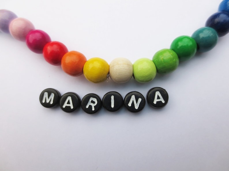 May include: A rainbow colored wooden bead necklace with the name "MARINA" spelled out in black letter beads.