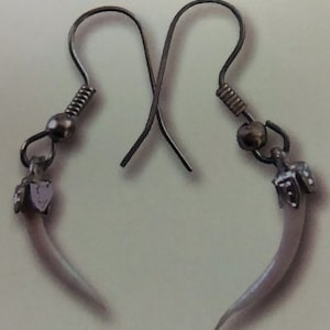 May include: A pair of silver earrings with a white tooth-shaped charm. The earrings have a simple hook design.