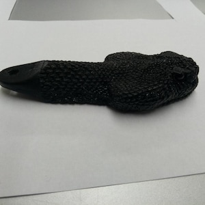 May include: Black rubber rattlesnake bottle opener with a textured surface.