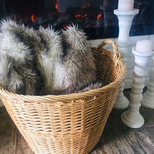 May include: A wicker basket with a faux fur throw blanket inside. The basket is sitting in front of a fireplace with white candle holders.