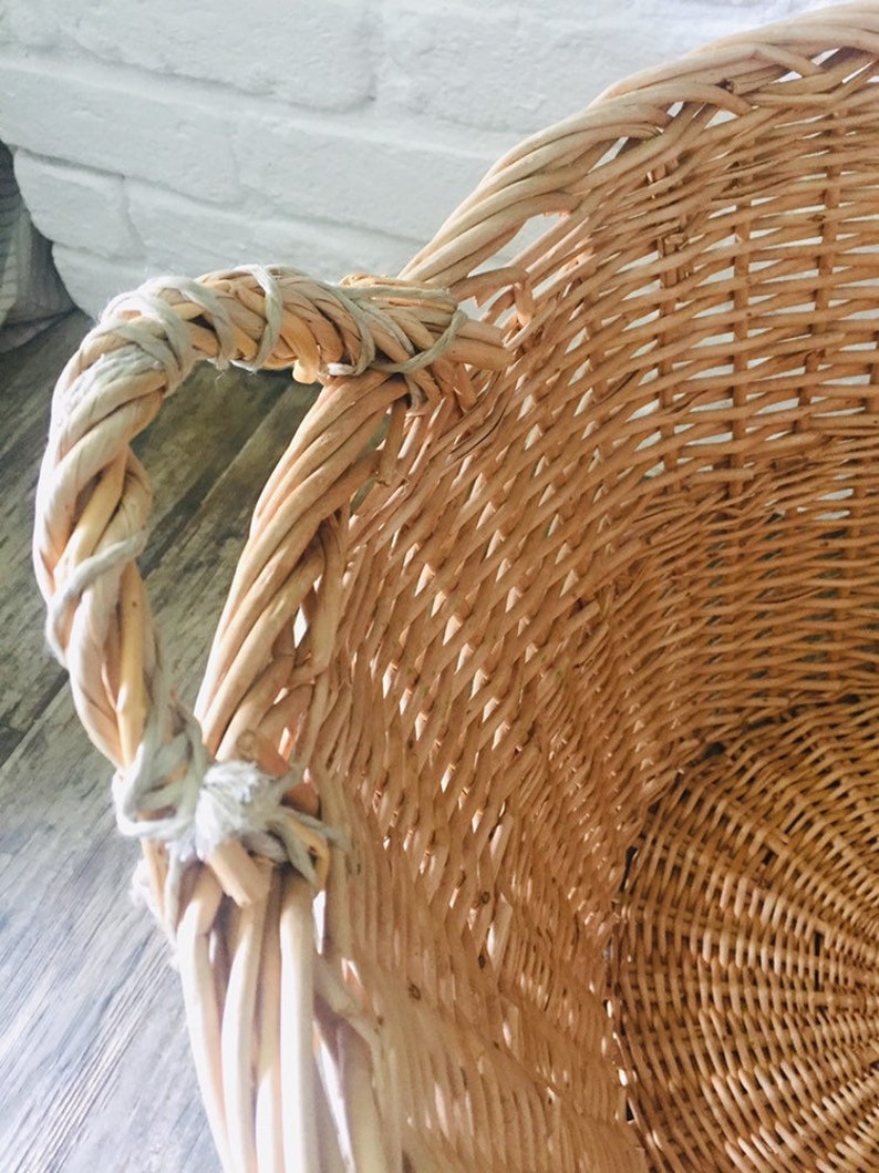 May include: A large, natural woven wicker basket with a single handle. The basket is made of light brown wicker and has a natural, rustic look.